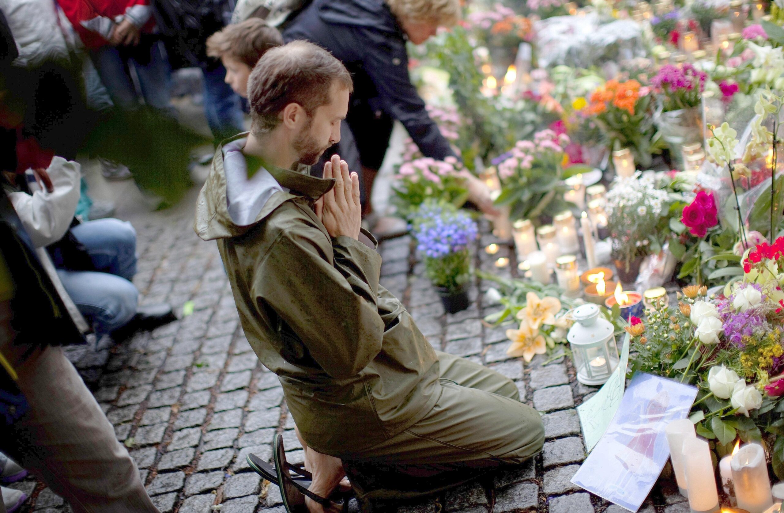 Wie lässt sich der Schmerz lindern: Ein Mann betet vor einem Meer aus Blumen für die Toten.