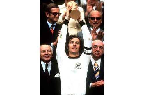 Franz Beckenbauer schnappt sich den Pokal und hält ihn für das Publikum im Münchener Olympiastadion in die Höhe.