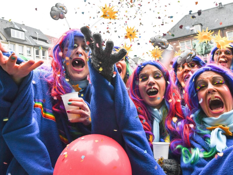 Verkleidete Jecken feiern an Altweiber in Düsseldorf und werfen mit Konfetti.