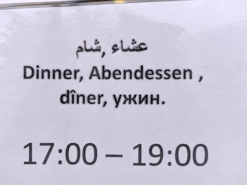  Ein mehrsprachiges Schild weist auf Essenszeiten für das Abendessen hin in der Mensa hin.