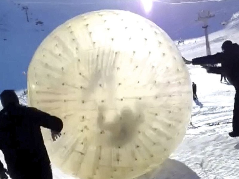 Zwei Mitarbeiter des Veranstalters geben der Zorbing-Kugel schwung, bevor diese dann den Berg herunter rollt.