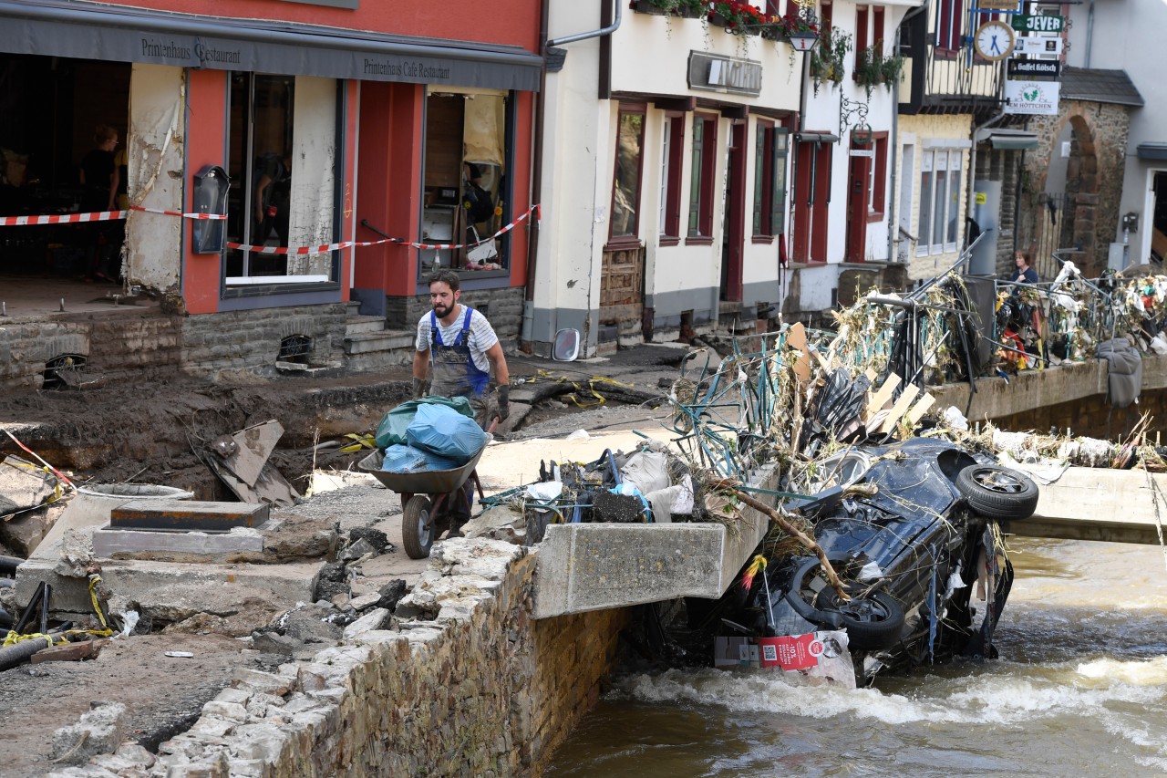 Nordrhein-Westfalen, Bad Münstereifel: Ein Helfer befördert Müll und Trümmer an der Erft entlang.