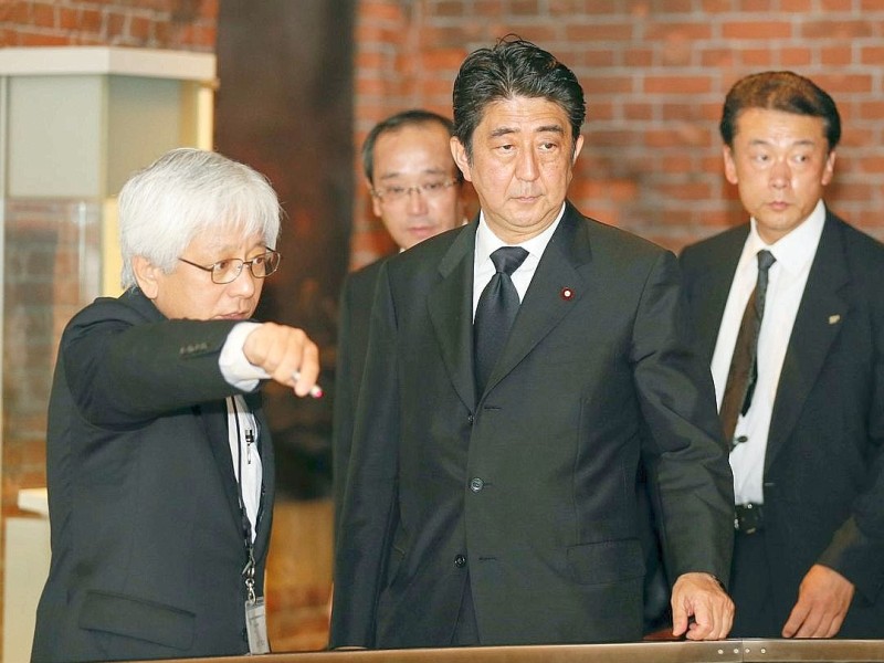 Viele Menschen gedenken  der Opfer des Atombombenabwurfs über Hiroshima vor 68 Jahren. Im Friedenspark steht noch immer eine Ruine als Mahnmal. Der Premierminister Japans, Shinzo Abe (Mitte), nimmt an den Gedenkfeierlichkeiten teil. Er unterhält sich mit Kenji Shiga (links), dem Direktor des Friedensmuseums Hiroshima.