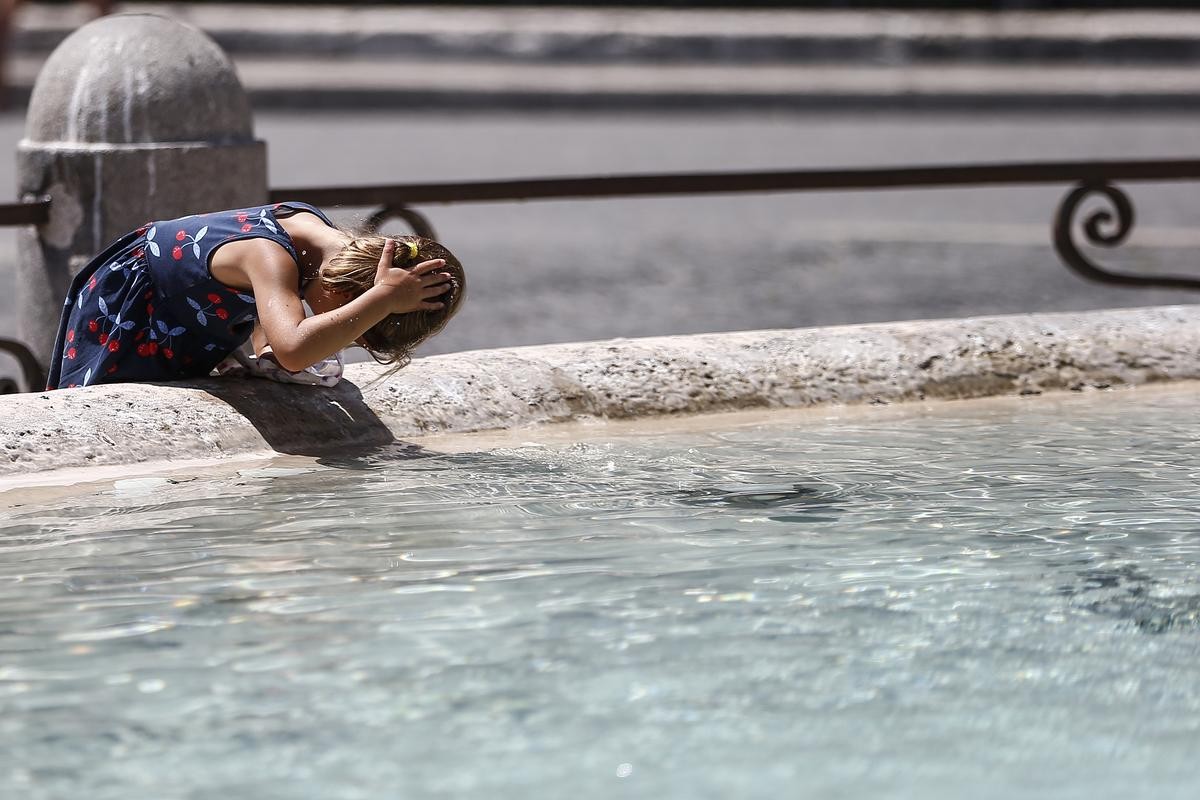 Ein Mädchen kühlt sich bei hohen Temperaturen den Kopf mit Wasser aus einem Brunnen. 