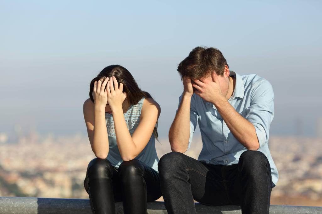 Ein Mann und eine Frau sitzen niedergeschlagen auf einer Mauer und stützen den Kopf in die Hände.