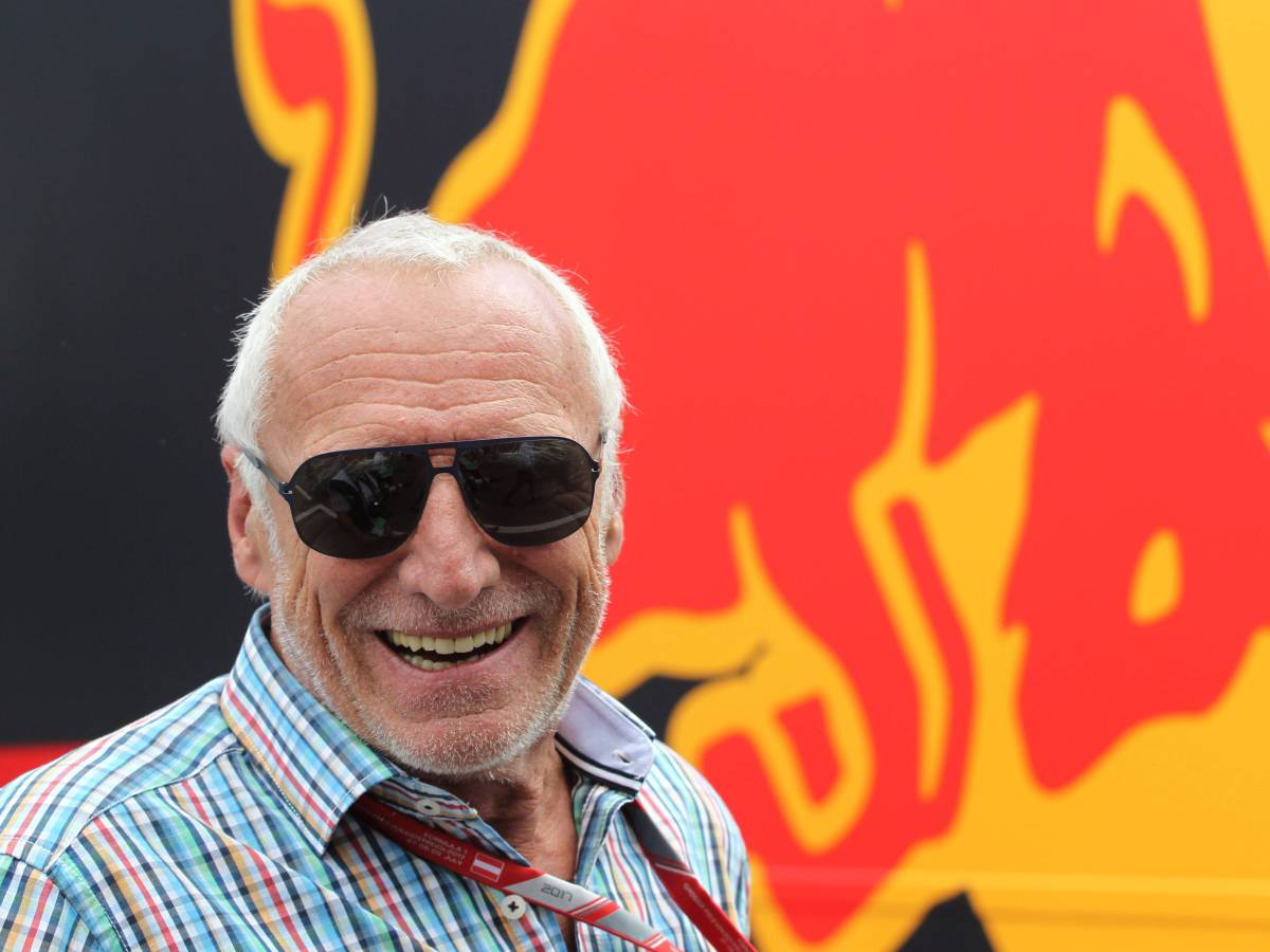 Dietrich Mateschitz lächelt vor dem Red-Bull-Logo in die Kamera.