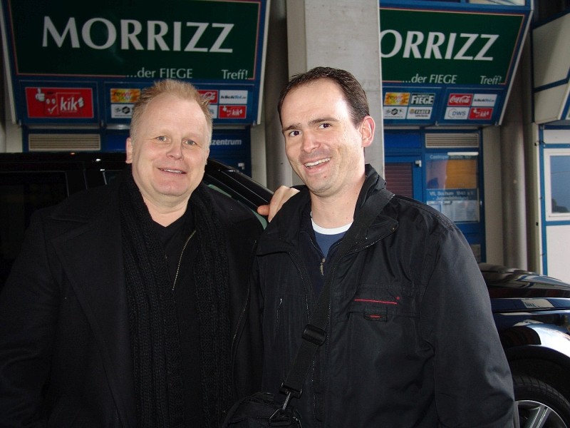 Kai Jansen: Das Foto zeigt Herbert Grönemeyer und mich am 4. November 2008 vor den VIP-Eingängen des Bochumer rewirpower-Stadions. An diesem Tag fand im Pressecenter des Stadions am Vormittag eine Pressekonferenz für das gemeinsame Konzert von Herbert Grönemeyer mit den Bochumer Symphonikern am 6. Juni 2009 im rewirpower-Stadion statt. Ich hatte am Morgen bei Radio Bochum gehört, dass an diesem Tag die Pressekonferenz im Stadion stattfinden sollte. Da ich am Vormittag keine weiteren Verpflichtungen hatte, bin ich zum Stadion gefahren, in der Hoffnung, dort Herbert Grönemeyer zu begegnen. Und ich hatte Glück! Um kurz vor 11 Uhr fuhr ein Wagen vor, aus dem ein überaus gut gelaunter Herbert Grönemeyer stieg. Neben mir waren noch zwei weitere Fans von ihm dort. Während man durch ein Fenster sehen konnte, wie die zahlreichen Journalisten und Fotografen im Presseraum auf Herbert Grönemeyer warteten, hat er sich erst einmal für uns Fans Zeit für ein nettes Gespräch und ein paar Fotos genommen. Ich erinnere mich, dass er mich auf die aktuellen VfL Bochum-Trikots angesprochen hat, die man im Fenster des Fanshops sehen konnte. Außerdem wollte er von mir wissen, was es mit der blauen Maus im Schaufenster des Fanshops, also mit Bobby Bolzer, dem Kindermaskottchen des VfL Bochum auf sich hat. Als ich ihm das erzählt habe, hat er sich köstlich amüsiert. Alles in allem war diese Begegnung mit einem ganz entspannten und überaus freundlichen Herbert Grönemeyer ein tolles Erlebnis.