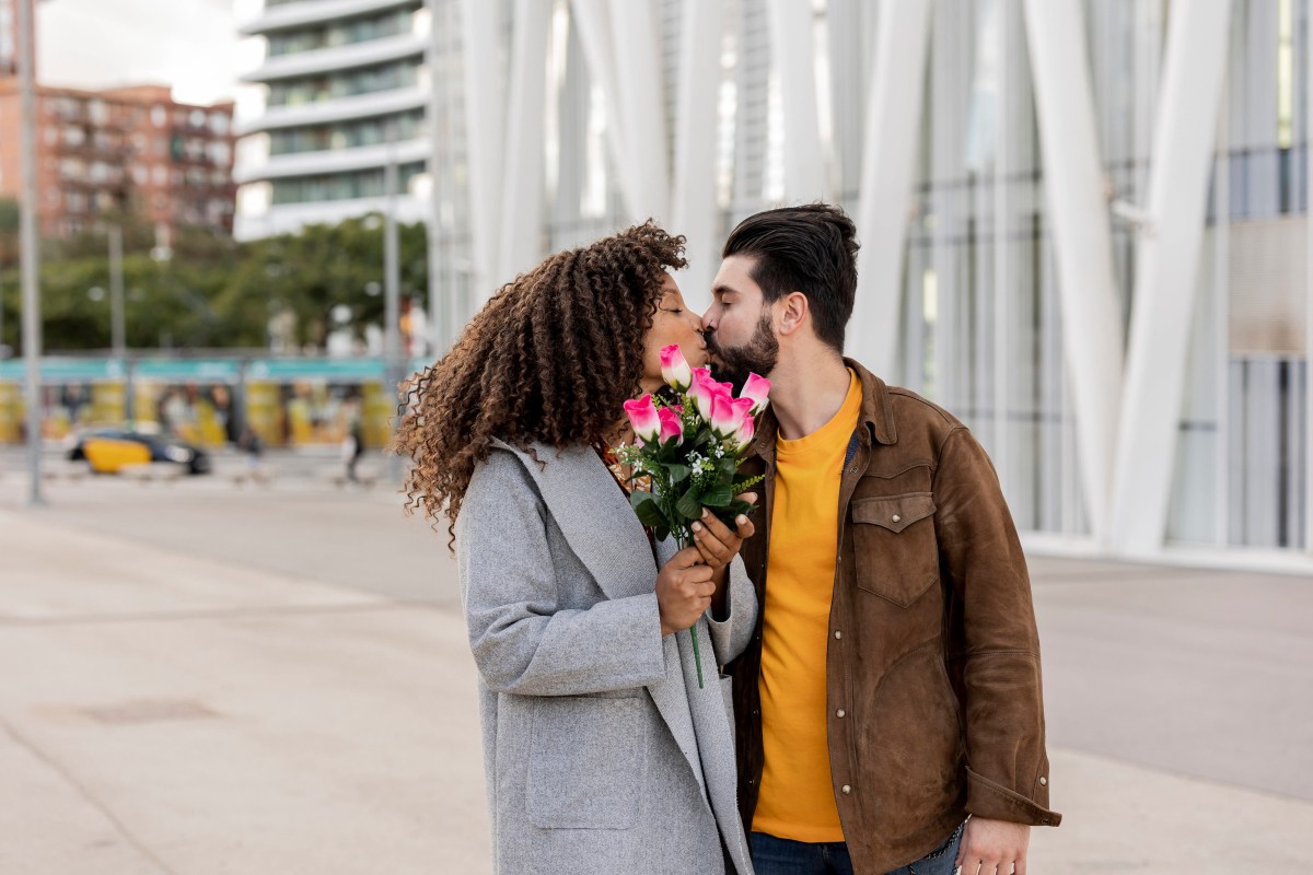 Sich küssendes Pärchen. Sie hält Blumen in der Hand, die sie von der Hochzeit träumen lassen.