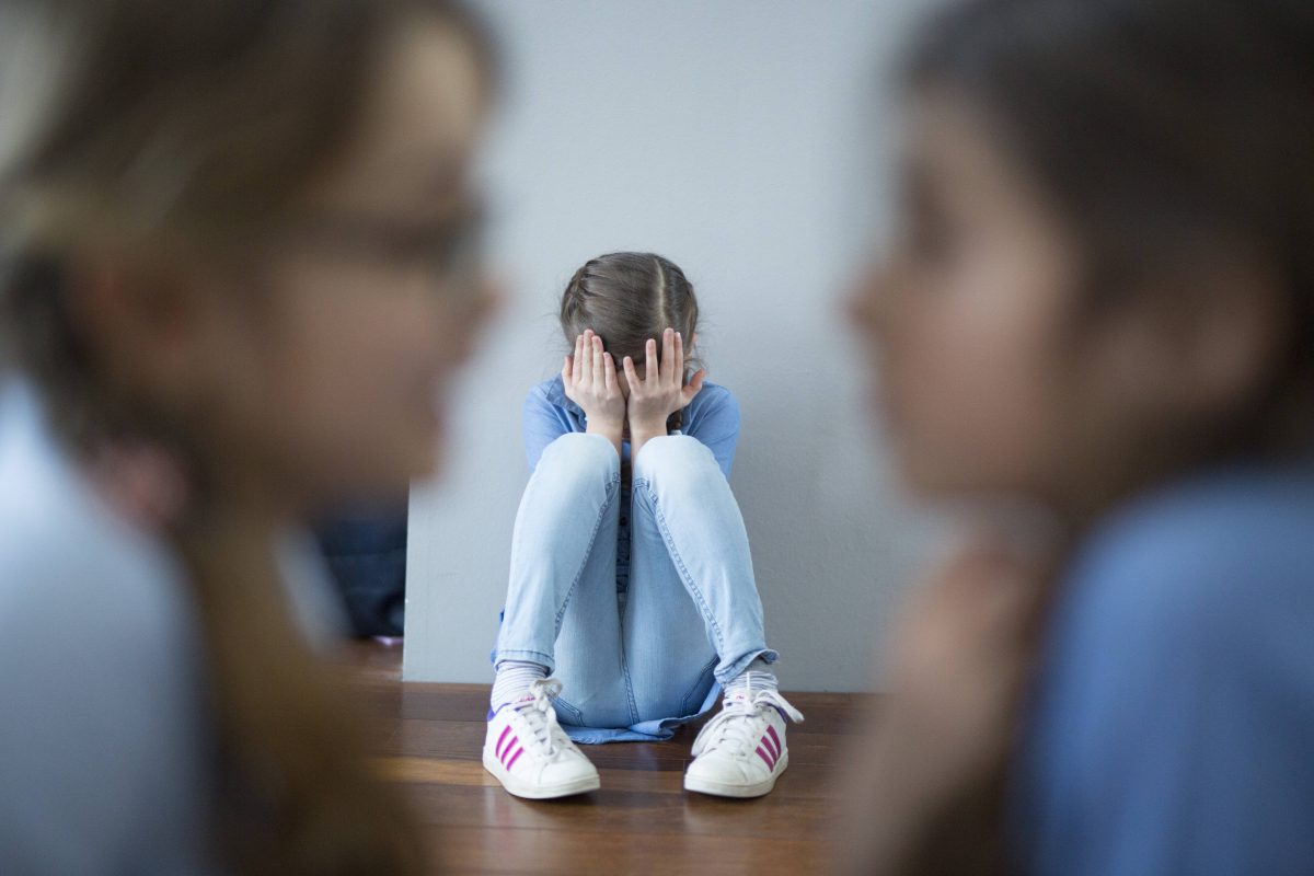 Mädchen mit Kopf in den Händen auf dem Boden sitzend