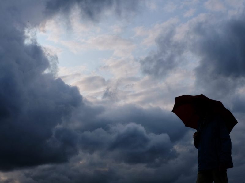 Person mit Regenschirm schaut in Gewitterhimmel