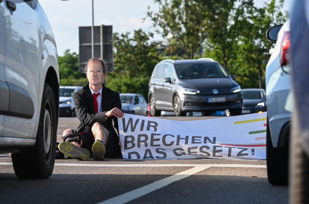 Aktivisten der "Letzten Generation" sitzen maskiert auf einer Straße