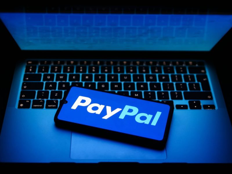 Paypal-App auf Smartphone, das auf einem aufgeklappten Laptop liegt