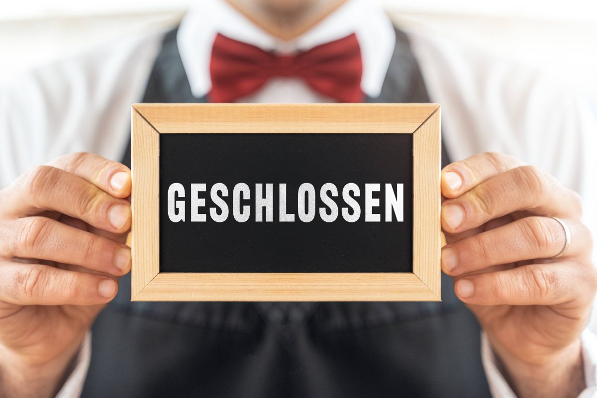 Kellner hält "Geschlossen"-Schild hoch