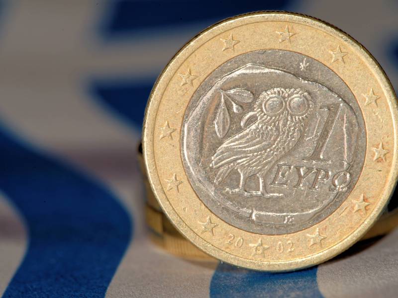 Eine 1-Euro-Münze aus Griechenland steht auf ihrem Rand, sodass die Rückseite mit der Eule zu sehen ist.