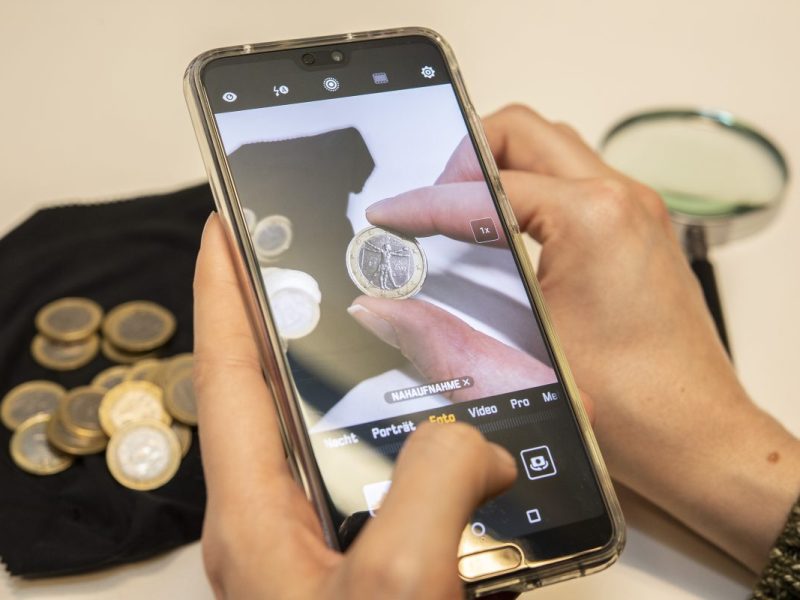 Eine Frau schaut sich auf einem Handy Euro-Münzen an.