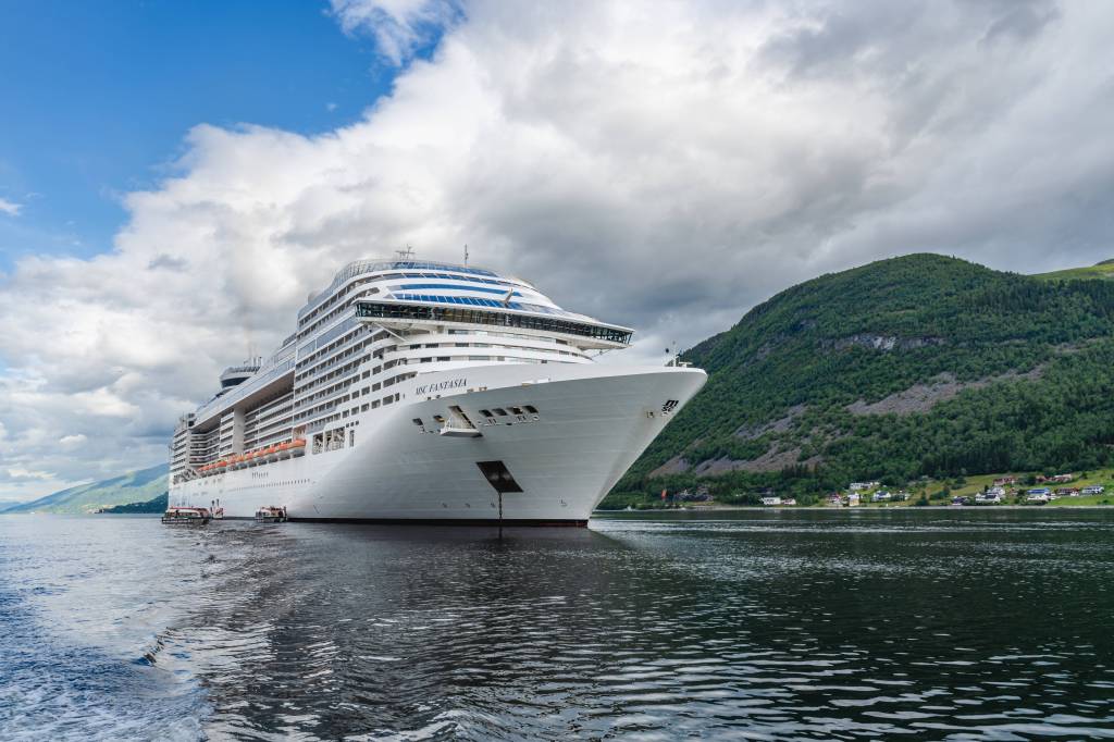 Ein Kreuzfahrtschiff vor grüner Landschaft.