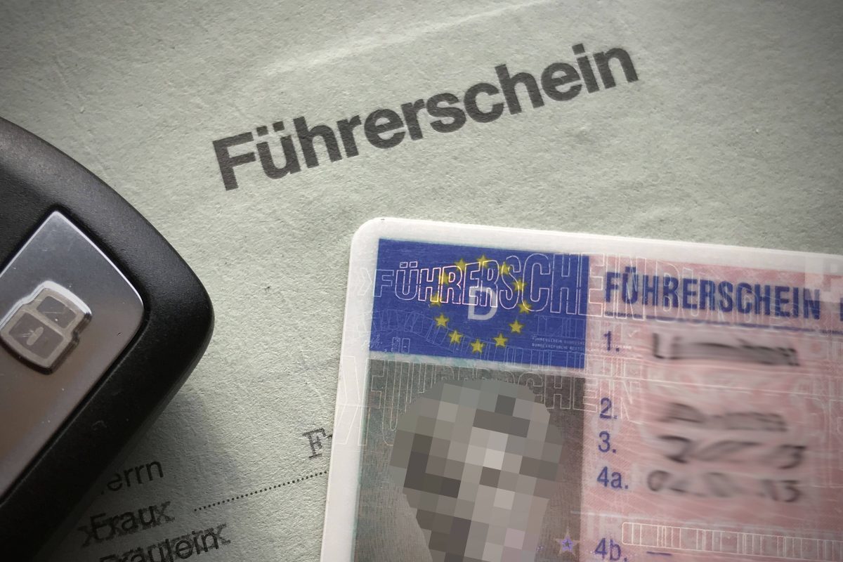 Ein weißes Blatt, auf dem in schwarz das Wort "Führerschein" steht. Auf dem Blatt liegt ein Führerschein, auf dem das Bild und der Name verpixelt ist. Oben rechts im Bild erkennt man einen schwarzen Autoschlüssel.