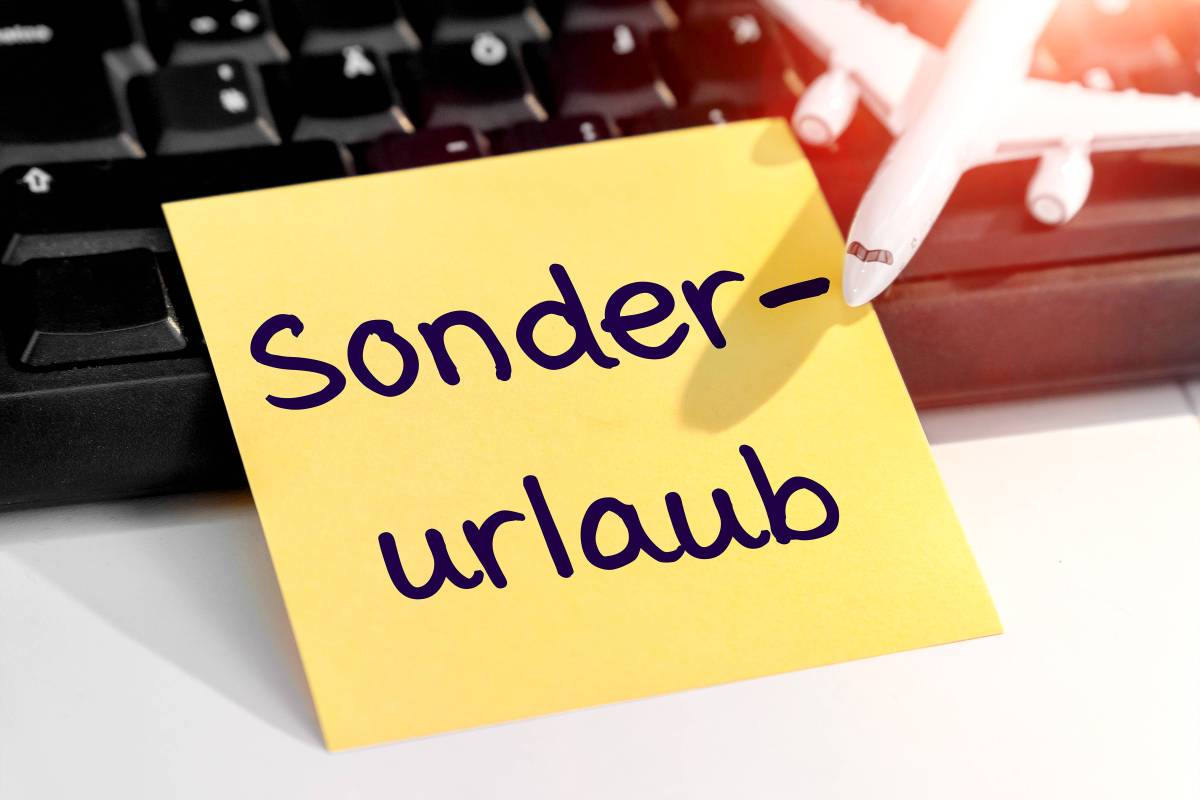 Auf einer schwarzen Tastatur ist ein gelber Zettel angelehnt. Auf dem Zettel steht mit schwarzer Schrift "Sonderurlaub". Oben Rechts im Bild ist außerdem ein weißes Flugzeug.