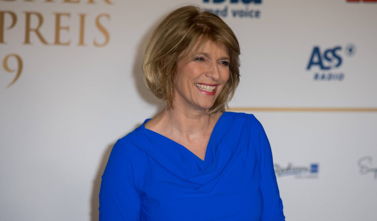 Auf dem Bild ist Tagesschau-Moderatorin Susanne Holst. Sie hat schulterlange blonde Haare. Zudem hat sie ein breites Grinsen im Gesicht und trÃ¤gt ein kÃ¶nigsblaues Kleid.
