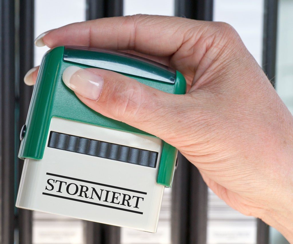 Eine Hand hält einen Stempel mit dem Aufdruck "storniert".