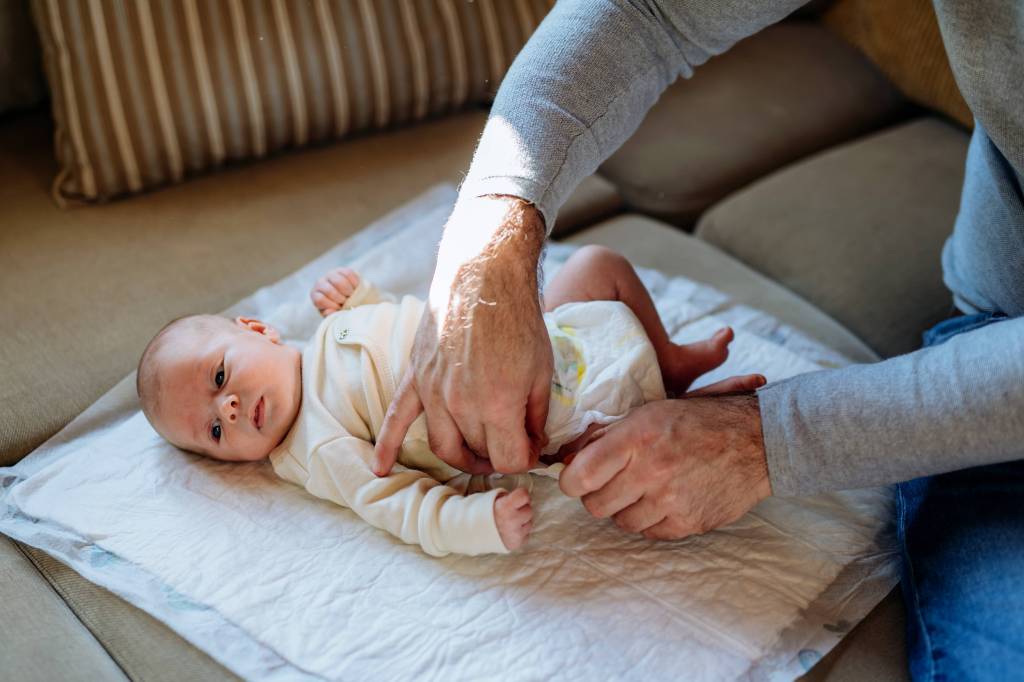Baby wird von Vater gewickelt.