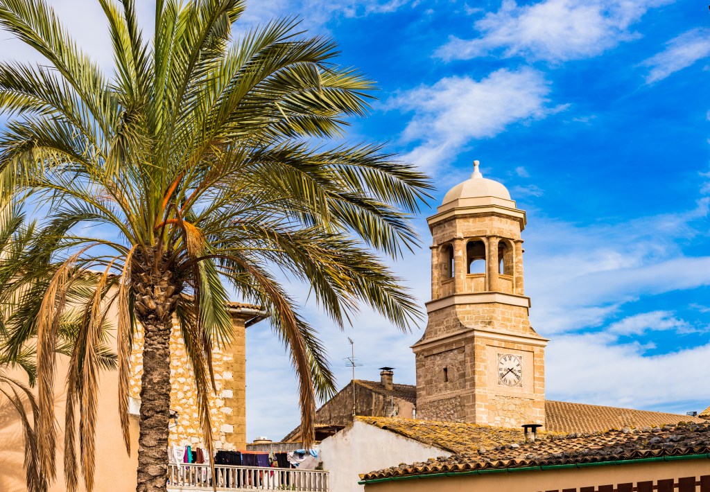 Kirchturm mit Palma in klarem Himmel.