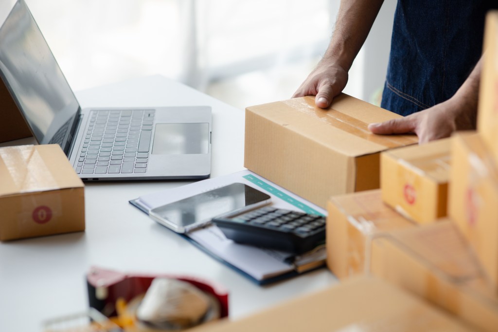 Eine Person mit einiger Ware in Paketen verpackt, die online verkauft wurde. Symbolbild für die Abgrenzung zwischen Privatverkäufer und gewerblichem Händler auf Kleinanzeigen.