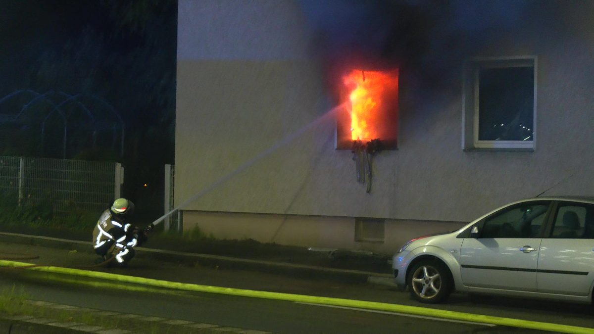 Wohnungsbrand in Essen: Ein Feuerwehrmann lÃ¶scht von auÃŸen durch das zerstÃ¶rte Fenster.