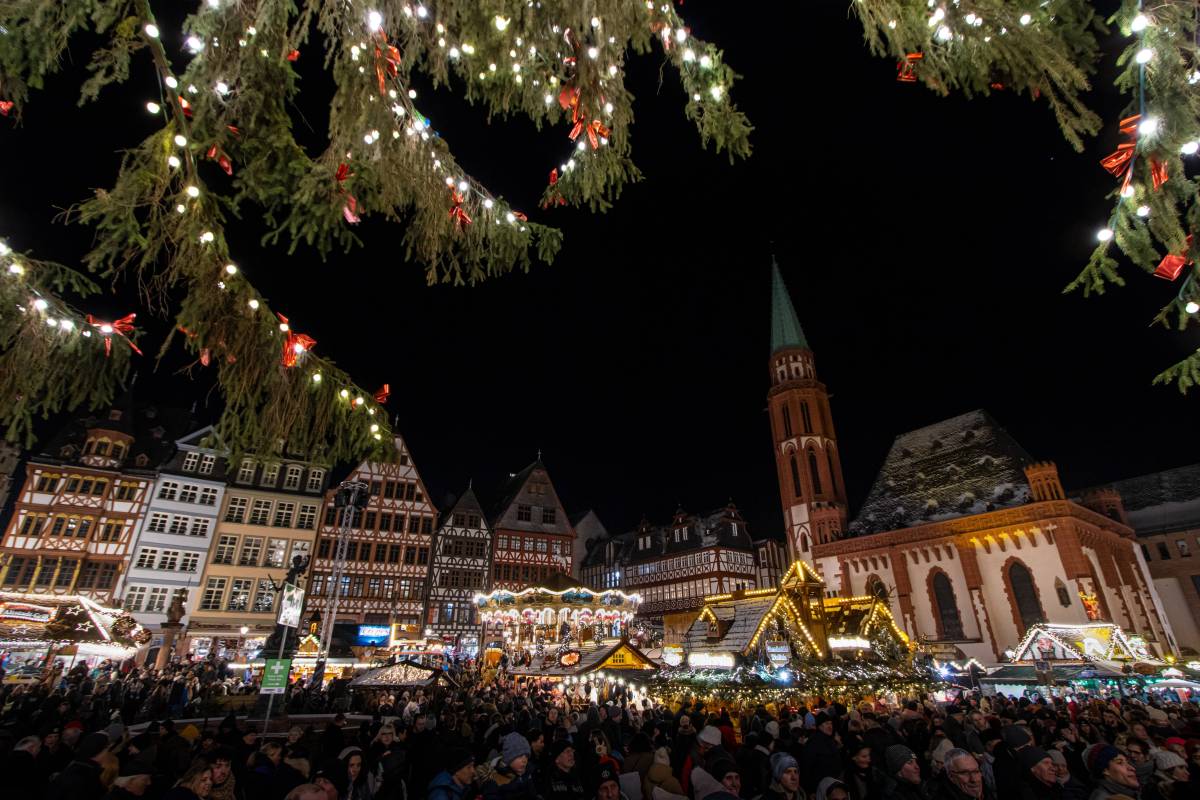 Ausblick auf groÃŸen Weihnachtsmarkt hinter Tannenzweigen.