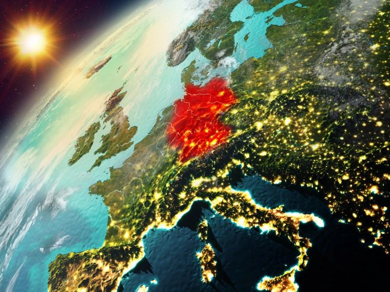Ein Blick aus dem Orbit auf die Erde hinter der die Sonne aufsteigt. Deutschland ist mit roter Farbe markiert.