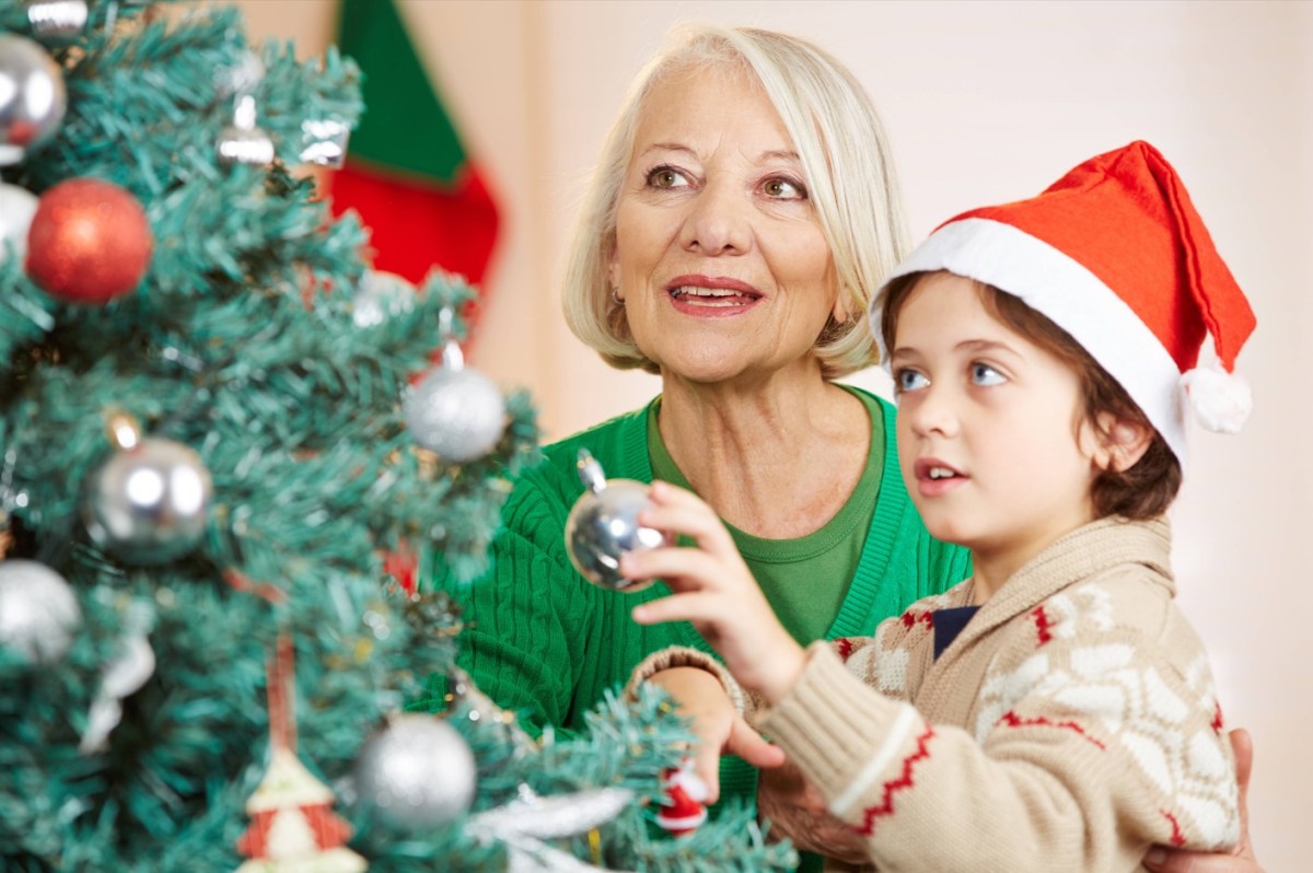 Ein kleiner Junge mit Weihnachtsmann-MÃ¼tze schmÃ¼ckt mit seiner Oma einen Weihnachtsbaum.