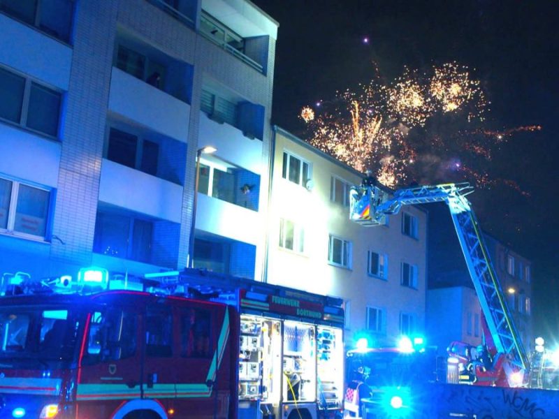 In Dortmund löschte die Feuerwehr einen Wohnungsbrand, ausgelöst durch eine Silvester-Rakete. Währenddessen erfüllt Feuerwerk den Himmel über der Stadt.
